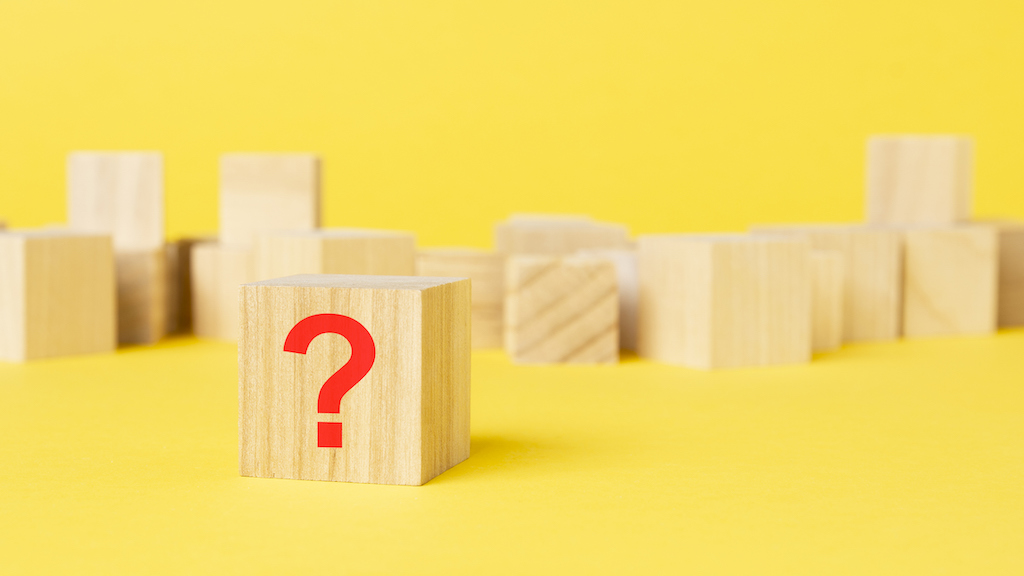 Red question mark on wooden block with yellow background. Representing FAQs about backup generator installation. 