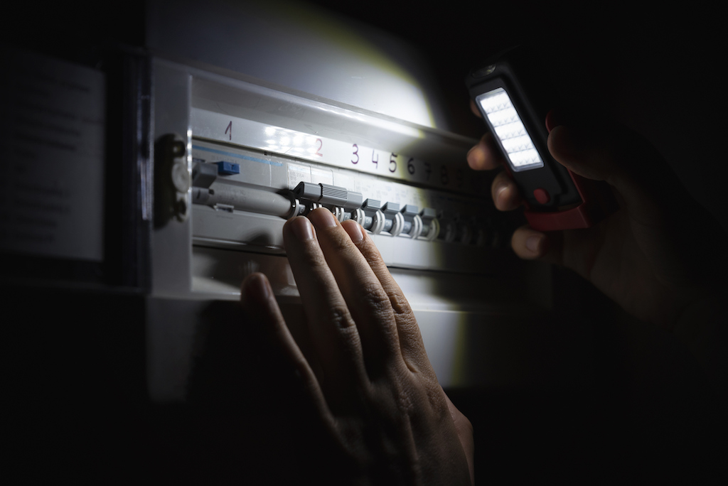 Person using a light to see their switchboard panel during power outage. They are in need of a backup generator install. 