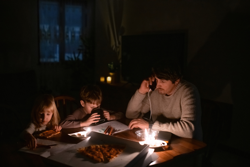 A man and his kids are sitting around candle light during a blackout. Calling emergency generator services.